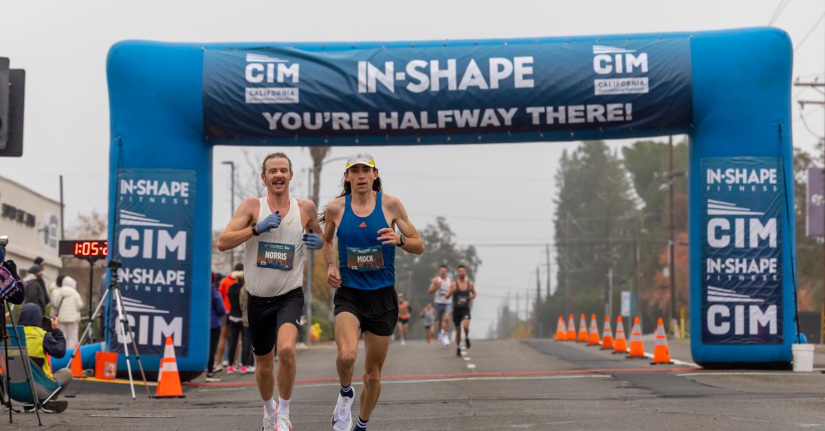 Two marathon runners competing in a foggy race reach the halfway mark under a blue archway.